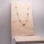 Clover and Pearl Station Necklace – Gold necklace with small stones on a beige stone display stand against a light grey background