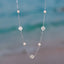Silver clover necklace with pearls against a blurred beach background