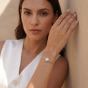 Halo Moissanite Bangle | 1ct VVS Moissanite | 925 Sterling Silver. A woman wearing a delicate silver bangle bracelet with a round pavé-set clear stone, posing against a textured beige wall.