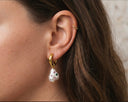 Close-up of an ear wearing gold hoop earrings with pearl-like charms.