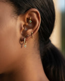 Close-up of a person's ear with gold earrings against a blurred background