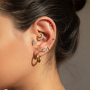 Close-up of an ear with multiple earrings on a neutral background