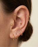 Close-up of an ear with multiple gold earrings on a neutral background