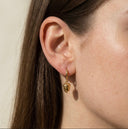 Close-up of a person wearing a gold earring with a green gemstone.