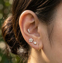 Close-up of an ear wearing multiple earrings with a blurred natural background