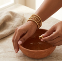 Person holding a terracotta bowl with gold beaded bracelet in a stack, showing its waterproof.