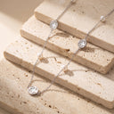 Amara Floral Pearl Station Necklace – Gold or Silver- A delicate silver chain necklace with three small clover-shaped silver pendants and three white pearl beads, displayed on stacked beige travertine stone blocks.