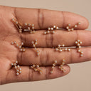 Zodiac Constellation CZ Flat Back Earring – 16G Push Pin Cartilage Stud-A close-up of a hand displaying multiple small gold-toned jewelry pieces arranged on the fingers against a plain beige background.