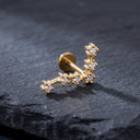 A gold-toned curved barbell stud earring decorated with multiple small clear cubic zirconia stones, displayed on a dark textured slate surface.