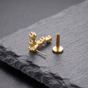A pair of gold-toned geometric stud earrings displayed on a dark gray slate surface, with one earring standing upright and the other lying on its side showing the post.