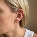Zodiac Constellation CZ Flat Back Earring – 16G Push Pin Cartilage Stud- Close-up of a person's ear showcasing multiple gold piercings, including a small hoop, two studs, a helix piercing with tiny clear stones, and a lobe piercing, against a soft beige background.