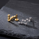 Zodiac Constellation CZ Flat Back Earring – 16G Push Pin Cartilage Stud- Two pairs of small stud earrings displayed on a dark slate surface: one pair in yellow gold and one pair in silver-tone metal, both with clear stones.