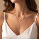Akuba Teardrop Necklace. A close-up of a woman wearing a delicate gold Y-necklace with a small teardrop pendant, paired with a white camisole top.