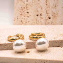 Gold hoop earrings with white pearls on a beige stone surface