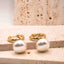 Gold hoop earrings with white pearls on a beige stone surface