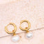 Gold hoop earrings with white pearls on a beige surface
