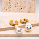 Gold hoop earrings with pearl-like pendants on a textured surface
