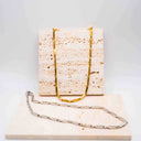 Gold and silver Sculpted Link Necklace in stainless steel. on a textured surface with a white background