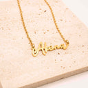 Gold necklace with 'Abena' pendant on a beige stone surface. Personalised Name Necklace – 18K Gold-Plated

Waterproof | Hypoallergenic | Made-to-Order