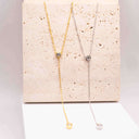 Moissanite Drop Pendant Necklace displayed in gold and silver on a textured background.