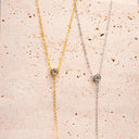Moissanite Drop Pendant Necklace displayed in gold and silver on a textured surface, showcasing elegance and style.