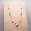 Clover and Pearl Station Necklace – Gold necklace with pearls and gemstones on a textured stone surface.