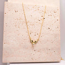 Gold necklace with a unique pendant on a textured beige card
