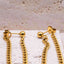 A close up Gold chain earrings on a textured beige surface