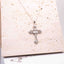Radiant Cross Necklace – Sterling Silver | Rhodium-Plated displayed on a textured surface.