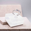 Hand with Twin Stone Sparkle Open Ring – Gold or Rhodium Plated on a blurred background. Silver ring with gemstones on a white stone surface