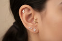 Close-up of an ear with gold and diamond earrings against a neutral background