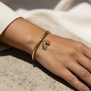 Acorn & Oak Leaf Open Bangle Gold bracelet on wrist with acorn and leaf charm on a textured surface