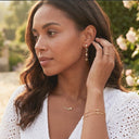 Woman adjusting her Ella & Faith London earrings outdoors with greenery in the background