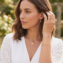 Woman wearing gold jewelry including earrings, necklace, and bracelet outdoors.