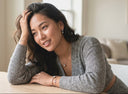 Woman in a grey sweater sitting on a couch in a bright room wearing Ella & Faith London Jewellery.