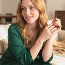Woman in a green dress sitting on a couch, wearing jewelry.