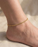 Gold anklet on a person's ankle against a neutral background