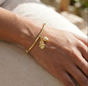 Gold bracelet with leaf and acorn design on a wrist against a neutral background