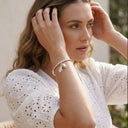 Woman wearing a silver Ella and Faith London acorn and leaf bangle, white lace top with a blurred background