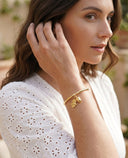 Woman wearing a gold acorn and leaf bracelet , outdoors.