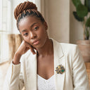 Woman wearing a white blazer with a brooch, sitting indoors.