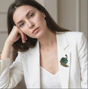 Woman wearing a white blazer with a decorative brooch, posing thoughtfully.