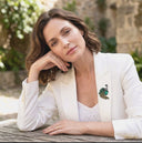 Woman in a white blazer with a brooch, sitting outdoors.