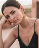 Woman wearing gold earrings with a blurred outdoor background