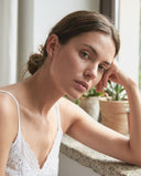 Woman in a white lace top sitting indoors with plants in the background