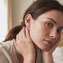 Woman wearing a silver earring, close-up of ear and hand.