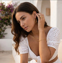 Woman wearing gold hoop earrings and rings, with a white top and floral background