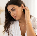 Woman wearing gold jewelry including earrings, a necklace, and a ring.
