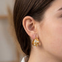 Close-up of a person wearing gold hoop earrings with pearl accents.