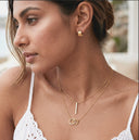 Close-up of a woman wearing gold necklaces and earrings outdoors.